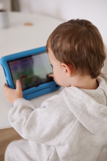 Niño feliz jugando en tableta digital en casa. Retrato de un niño en casa viendo dibujos animados en la tableta. Tecnología moderna para niños y educación.