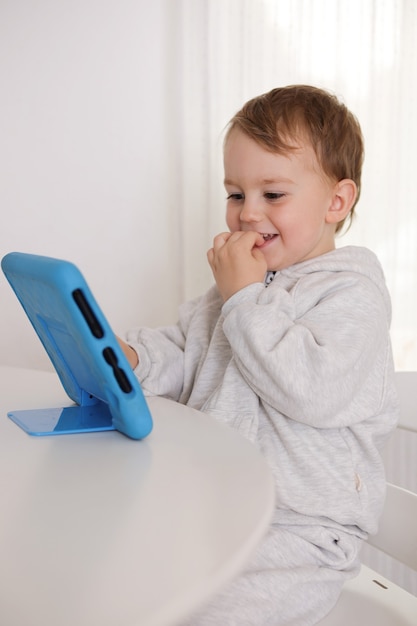 Niño feliz jugando en tableta digital en casa. Retrato de un niño en casa viendo dibujos animados en la tableta. Tecnología moderna para niños y educación.