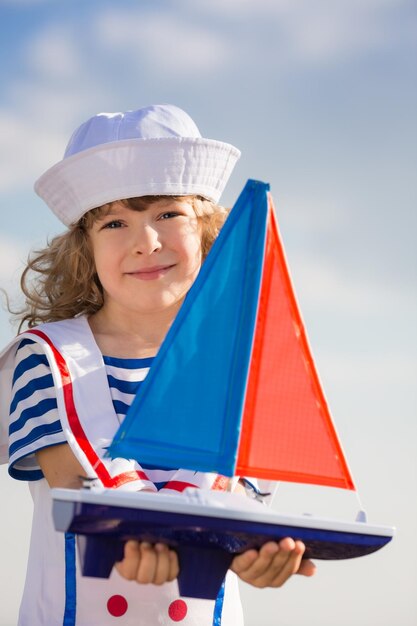 Niño feliz jugando con un velero de juguete contra el fondo del cielo azul