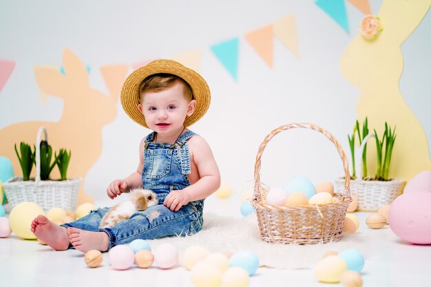 Niño feliz con lindo conejito esponjoso cerca de huevos de Pascua pintados