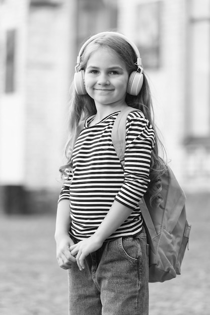 Niño feliz llevar bolsa de viaje escuchando música en auriculares modernos con estilo de moda casual estilo de vida urbano al aire libre