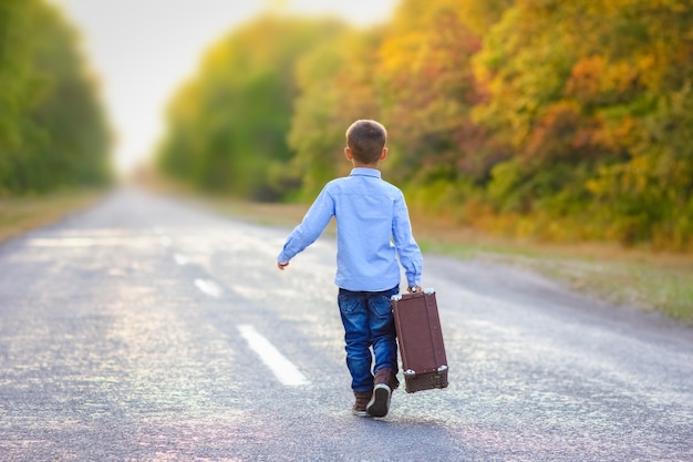 Un niño feliz con una maleta en la carretera en el viaje del parque