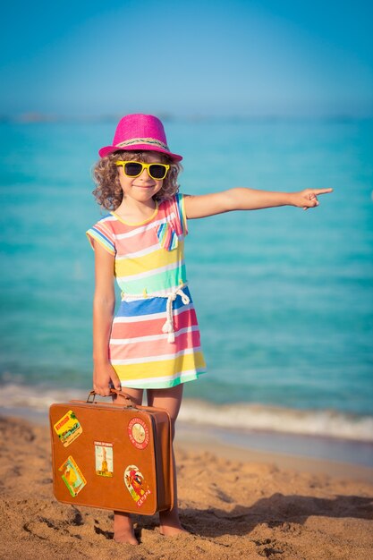 Foto niño feliz con maleta vintage en la playa