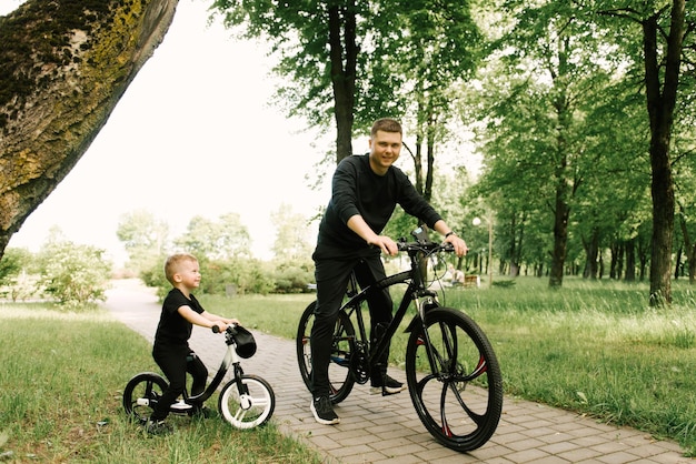 Un niño feliz monta una bicicleta con un padre joven en el parque