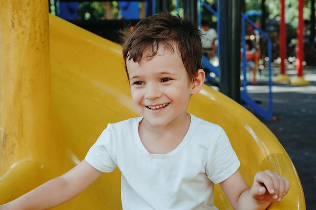 niño feliz monta un tobogán en el patio de recreo en verano