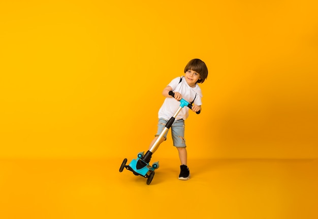 Niño feliz montando un scooter sobre una superficie amarilla con espacio para texto