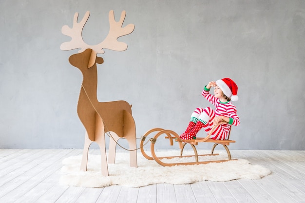 Niño feliz montando trineo de Navidad. Niño divirtiéndose en casa