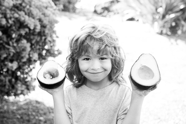 Niño feliz mostrando aguacate en el jardín de verano para niños comida sana