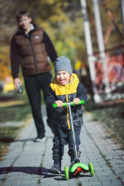 Un niño feliz en una moto camina por el parque con su padre en un día de otoño