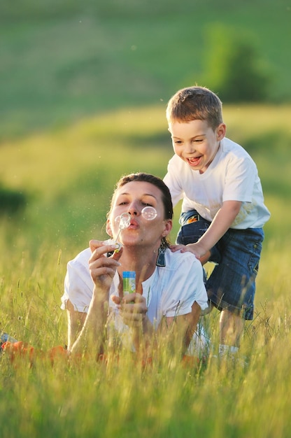 niño feliz y mujer jugando al aire libre con pompas de jabón en la pradera