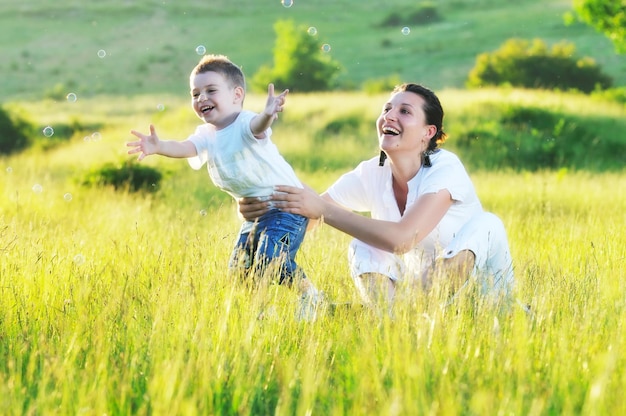 niño feliz y mujer jugando al aire libre con pompas de jabón en la pradera