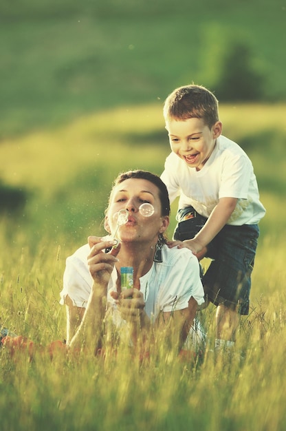 niño feliz y mujer jugando al aire libre con pompas de jabón en la pradera