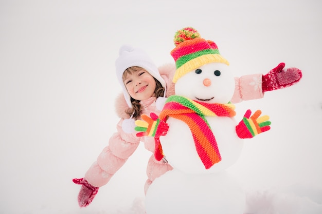 Niño feliz y muñeco de nieve en el parque de invierno