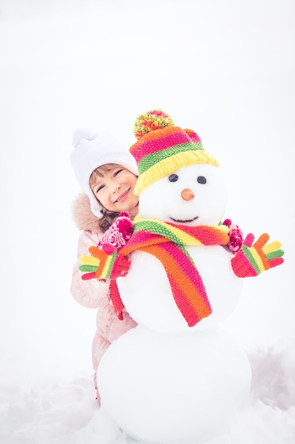 Niño feliz y muñeco de nieve en el parque de invierno