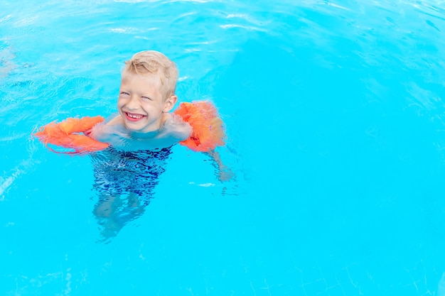 Niño feliz nada o aprende a nadar en la piscina de agua azul en brazaletes, el concepto de vacaciones de verano y vacaciones escolares