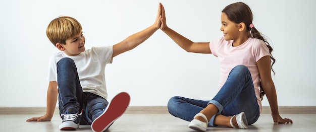 Foto el niño feliz y una niña sentados en el suelo y gesticulando