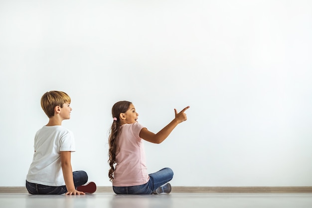El niño feliz y una niña sentados en el suelo y mostrando en la pared.