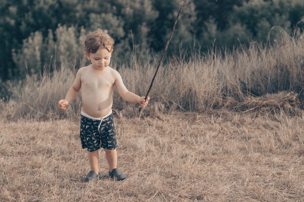 Niño feliz, niño jugando, mirada pensativa y sosteniendo en las manos el palo al aire libre