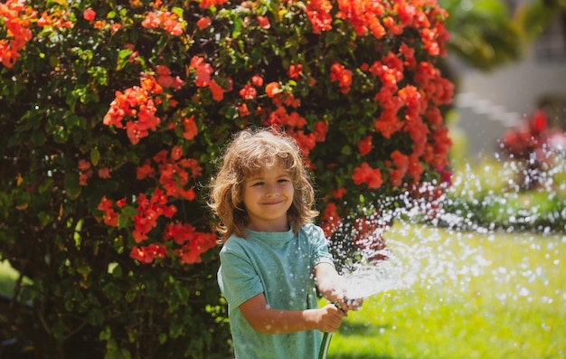 Niño feliz niño vierte agua de una manguera niño regando flores en el jardín jardinería doméstica