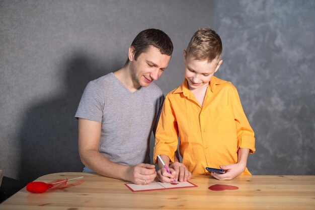 Niño feliz y papá firman una tarjeta de San Valentín y se ríen