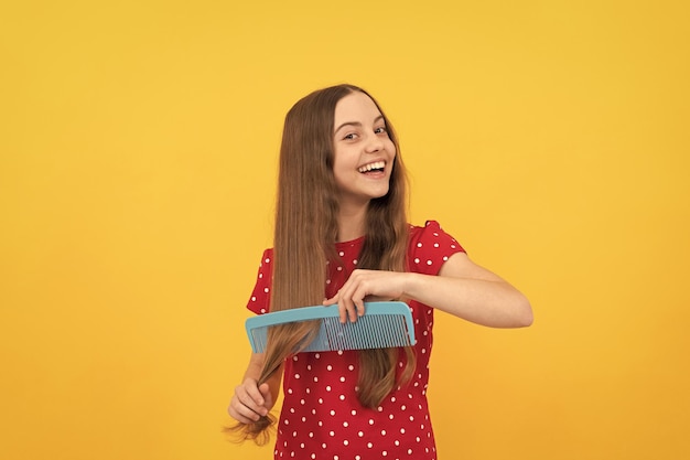 Niño feliz peinando el cabello largo en el cuidado del cabello de fondo amarillo