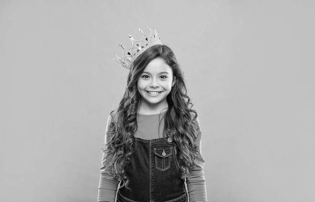 Niño feliz con el pelo rizado en la corona de la reina sobre el egoísmo de fondo azul