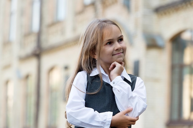 Niño feliz perdido en pensamientos con mirada pensativa en uniforme escolar al aire libre pensando