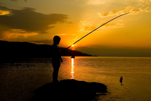 Niño feliz pescando junto a la silueta del mar