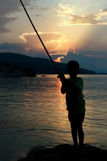 Foto niño feliz pescando en la silueta del mar