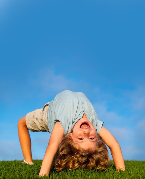 Niño feliz de pie boca abajo sobre la hierba verde Niño riéndose divirtiéndose en el parque de primavera Concepto de estilo de vida de niños saludables Niño deportivo haciendo ejercicio Cara de expresión