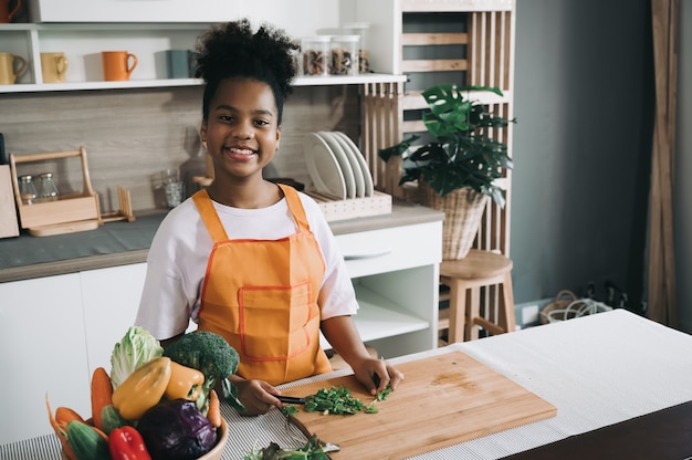 Niño feliz piel negra con ensalada de verduras en la cocina