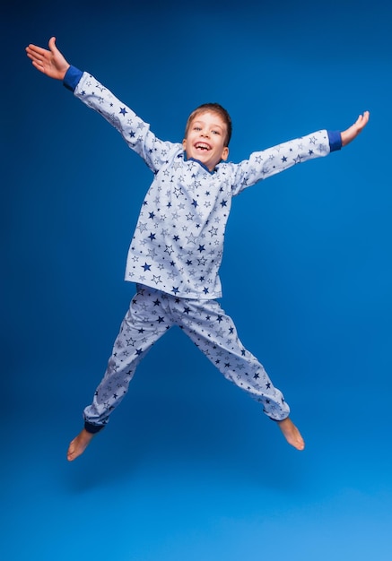 Un niño feliz en pijama salta sobre un fondo azul aislado el concepto de fotos de sueño para wildberris