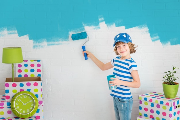 Foto niño feliz pintando la pared de color azul. niño divirtiéndose en casa. concepto de renovación de primavera