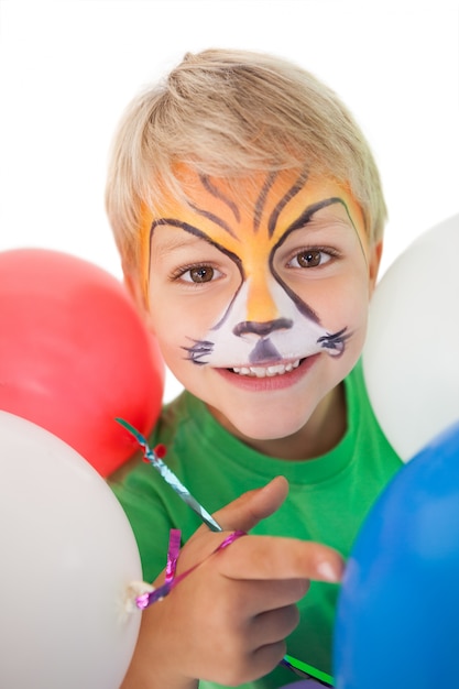 Niño feliz en pintura de cara de tigre con globos