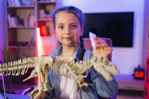 Un niño feliz de preescolar pegando huesos haciendo un modelo de tiranosaurio en la noche en casa