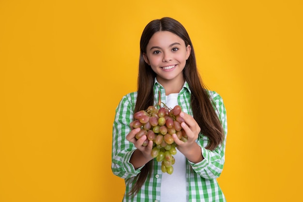 Niño feliz con racimo de uvas frescas sobre vitaminas de fondo amarillo