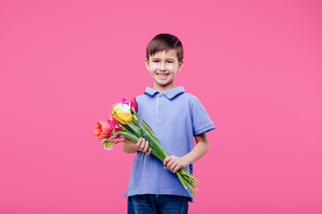 Niño feliz con un ramo de tulipanes aislado en la pared rosa