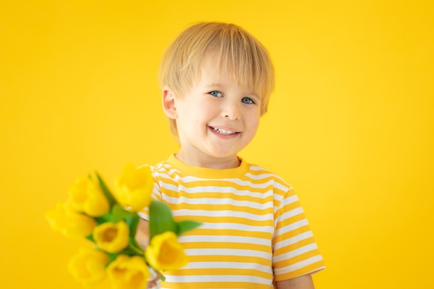 Niño feliz con ramo de tulipanes de primavera contra la pared amarilla.