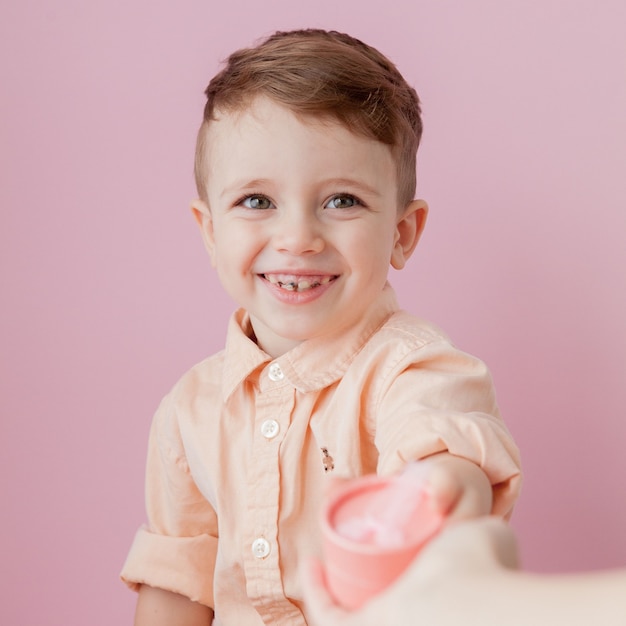 Niño feliz con un regalo. Foto aislada en pared rosa. El muchacho sonriente sostiene la caja actual. Concepto de vacaciones y cumpleaños.