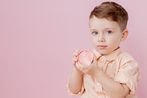 Niño feliz con un regalo. Foto aislada sobre fondo rosa. Niño sonriente tiene caja actual. Concepto de vacaciones y cumpleaños