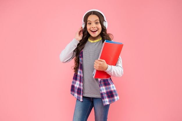 Niño feliz de regreso a la escuela escuchando un curso de audio en auriculares con fondo rosa, aprende.