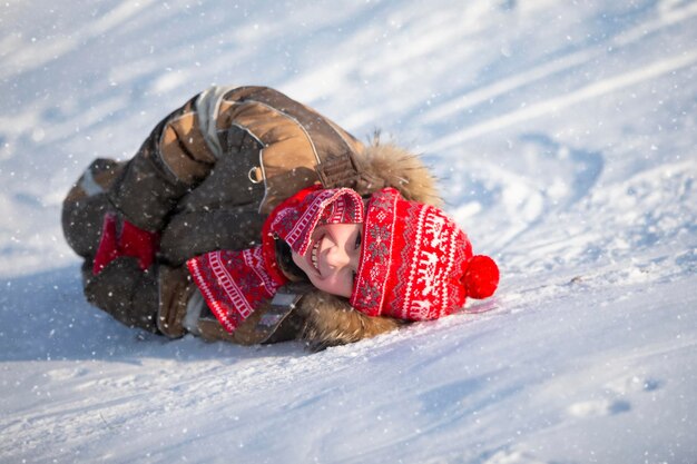 Un niño feliz con ropa de invierno yace en la nieve