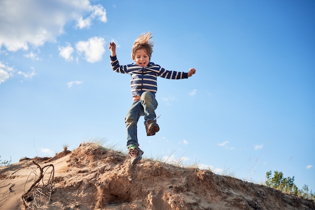 Niño feliz saltando sobre la arena en un día soleado