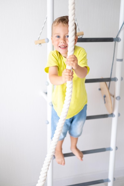 Niño feliz y saludable hace deportes en la pared sueca de la casa estilo de vida saludable deportes en casa complejo deportivo infantil escalera