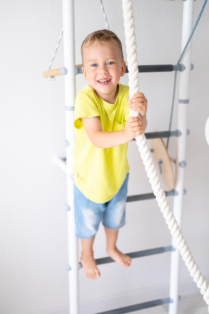 Niño feliz y saludable hace deportes en la pared sueca de la casa estilo de vida saludable deportes en casa complejo deportivo infantil escalera