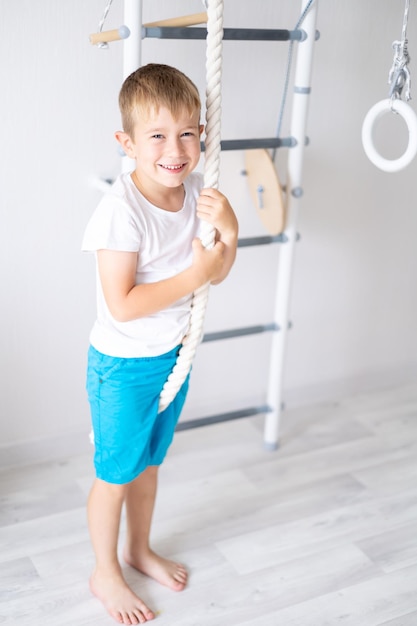 Foto niño feliz y saludable hace deportes en la pared sueca de la casa estilo de vida saludable deportes en casa complejo deportivo infantil escalera