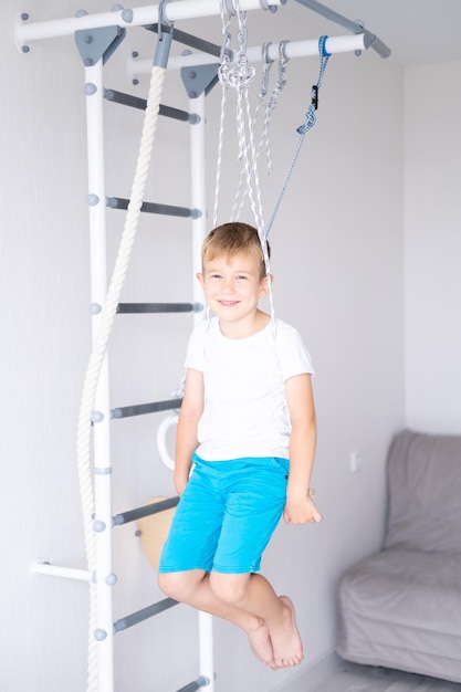 Niño feliz y saludable hace deportes en la pared sueca de la casa estilo de vida saludable deportes en casa complejo deportivo infantil escalera