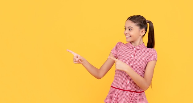 Niño feliz señalando con el dedo el anuncio del espacio de copia de fondo amarillo