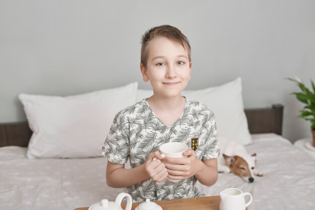 Niño feliz sentado en la cama y beber té.