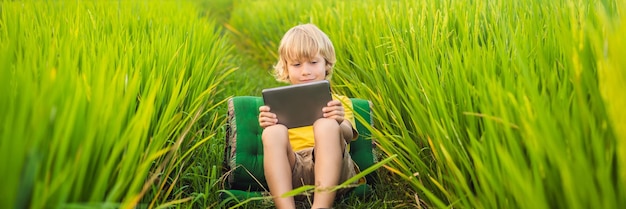 Niño feliz sentado en el campo sosteniendo tablet boy sentado en el césped en la escuela en casa día soleado